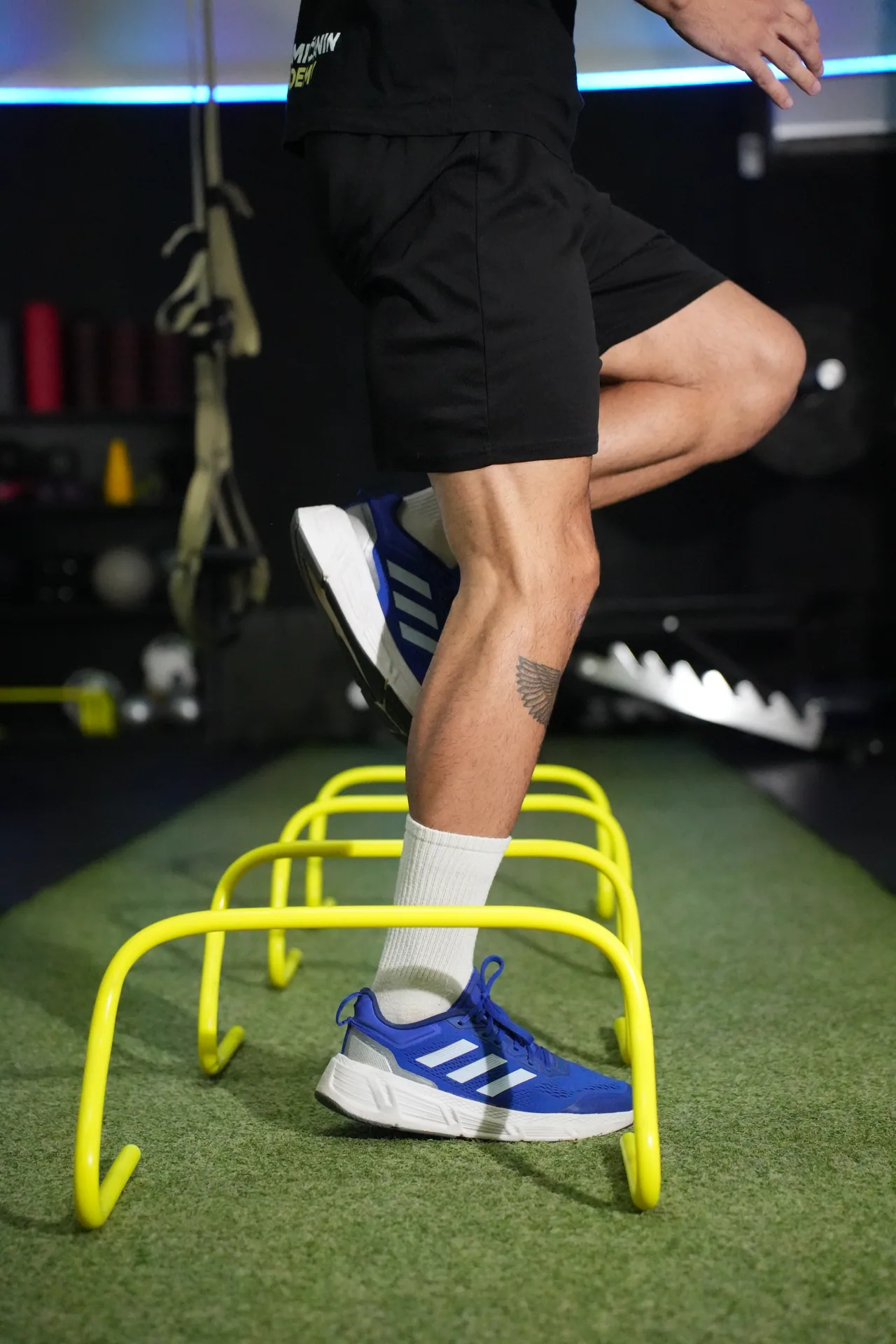 A footballer performs a speed and agility drill over low hurdles.